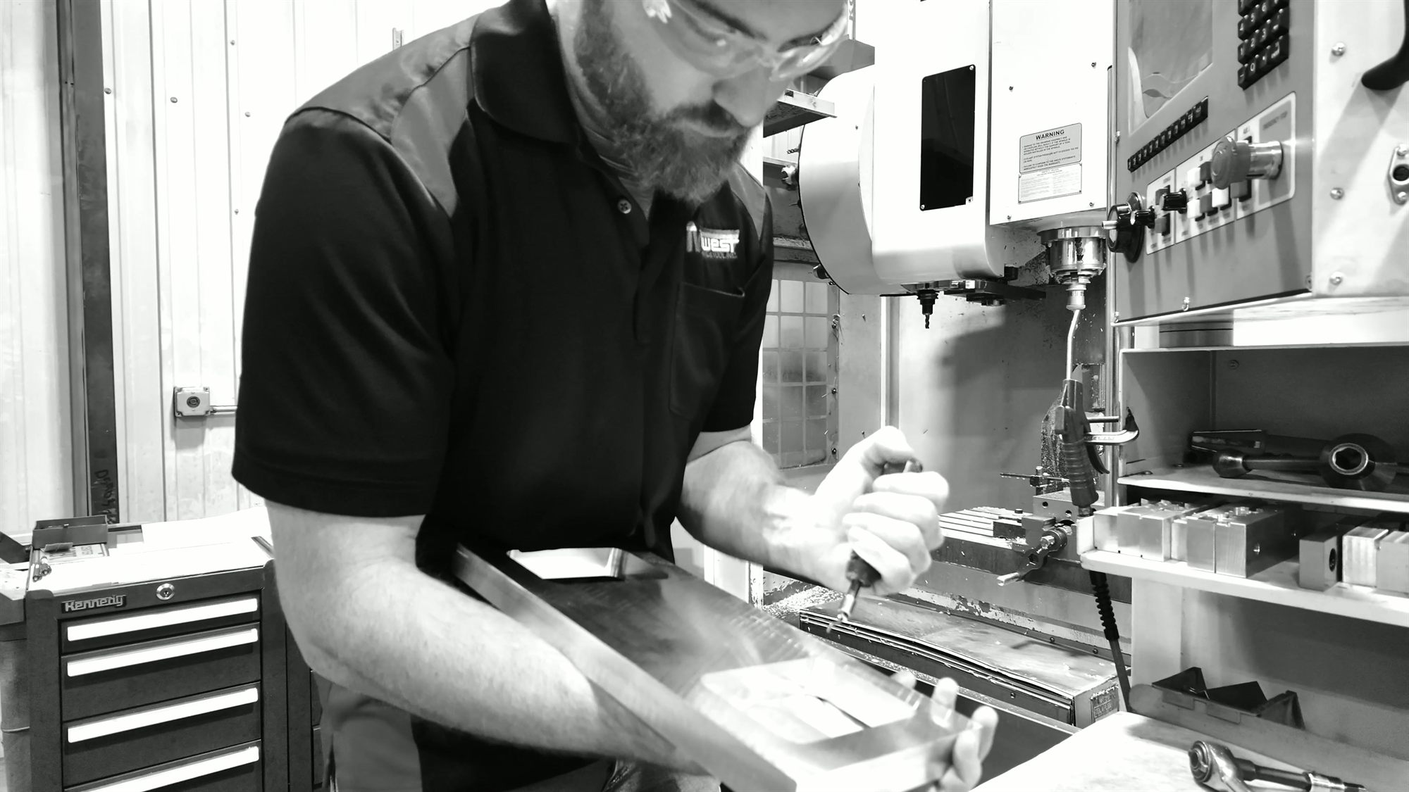 A machinist in safety glasses inspects a freshly machined part